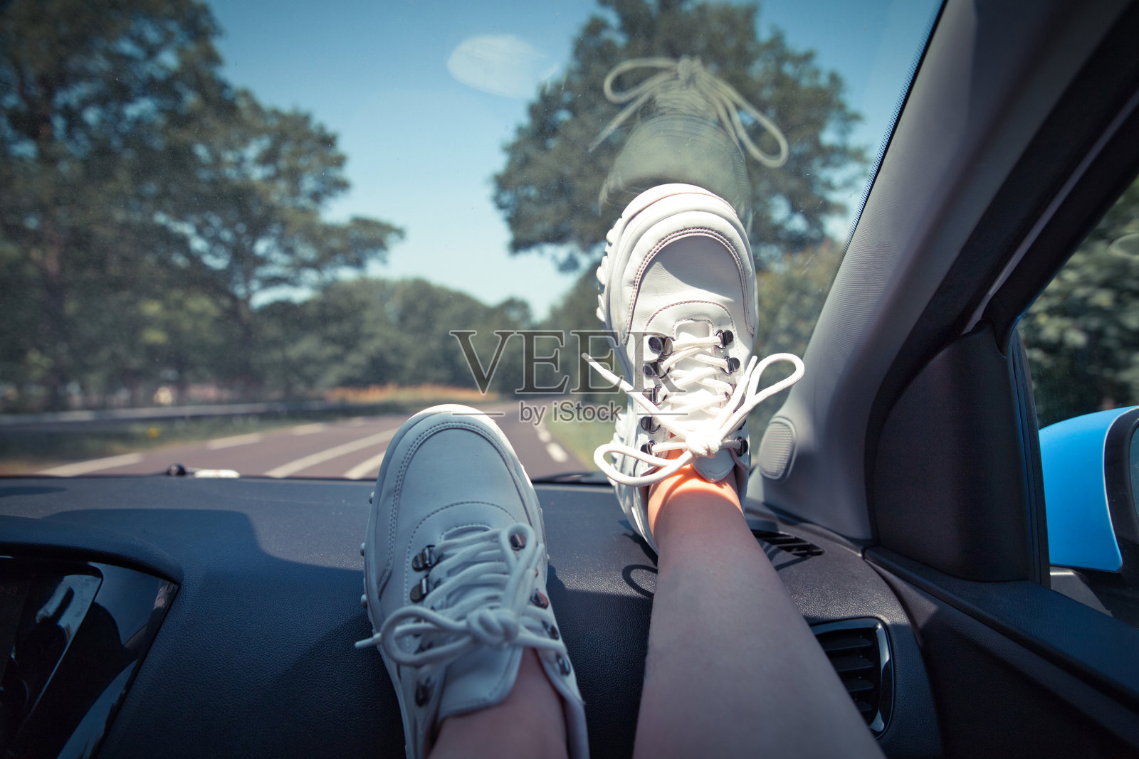 自由汽车旅行概念-女人放松与脚在仪表盘上穿着白色运动鞋。车里的性感女人。照片摄影图片