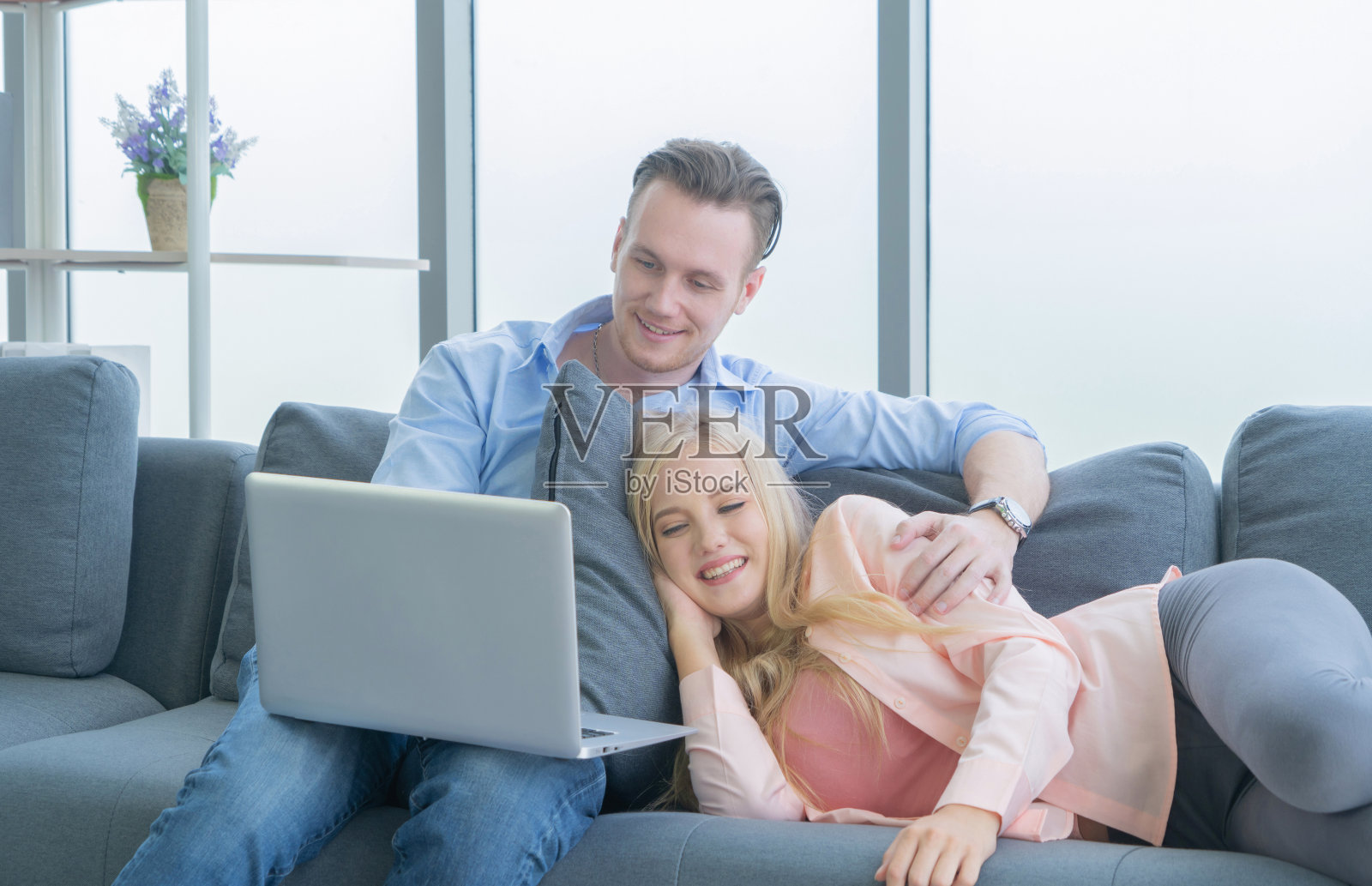 微笑的商务金发，白色夫妇放松和看电影在沙发上，花时间在一起隔离冠状病毒的概念。照片摄影图片