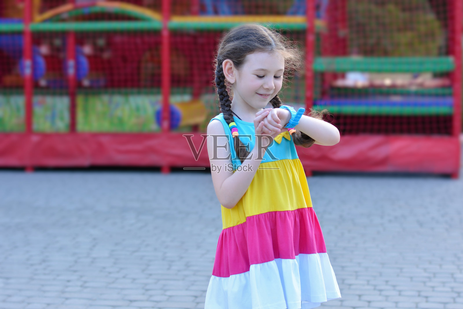 可爱美丽的小女孩脸上带着微笑，在街上对着智能手表说话。安全的概念照片摄影图片