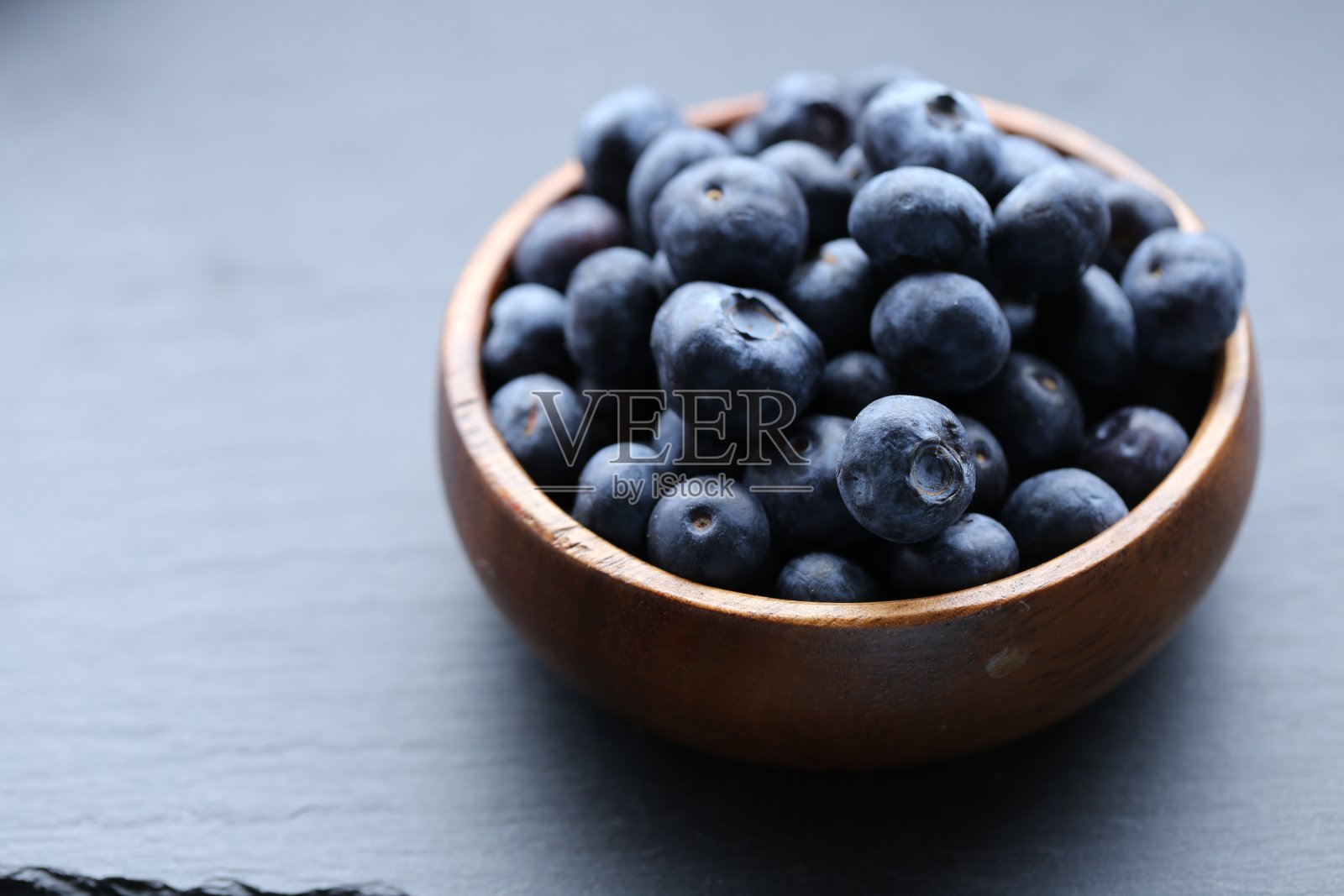 蓝莓莓在一个木制的圆杯特写在一个黑色的石板背景。健康的天然点心。素食和纯素食品。蓝莓的季节。照片摄影图片