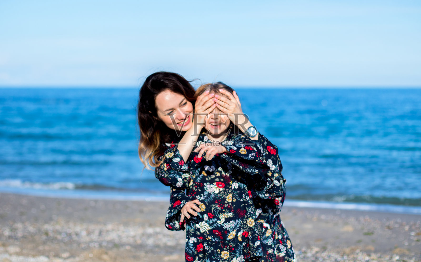 小女孩，年轻女子用双手捂住了眼睛。在沙滩上。类似的衣服照片摄影图片