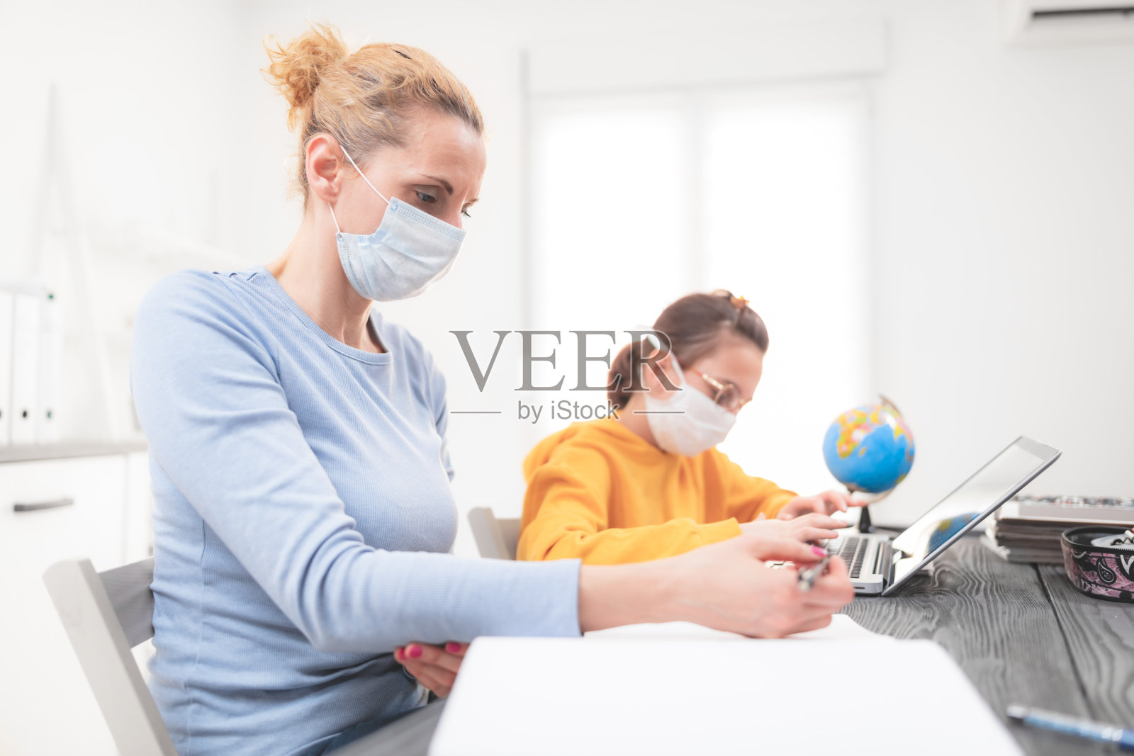 儿童在家学习教育，在家上学，在病毒、流感和季节性大流行时带着私人家教/母亲防护口罩，在社会接触中采取健康的方法。照片摄影图片