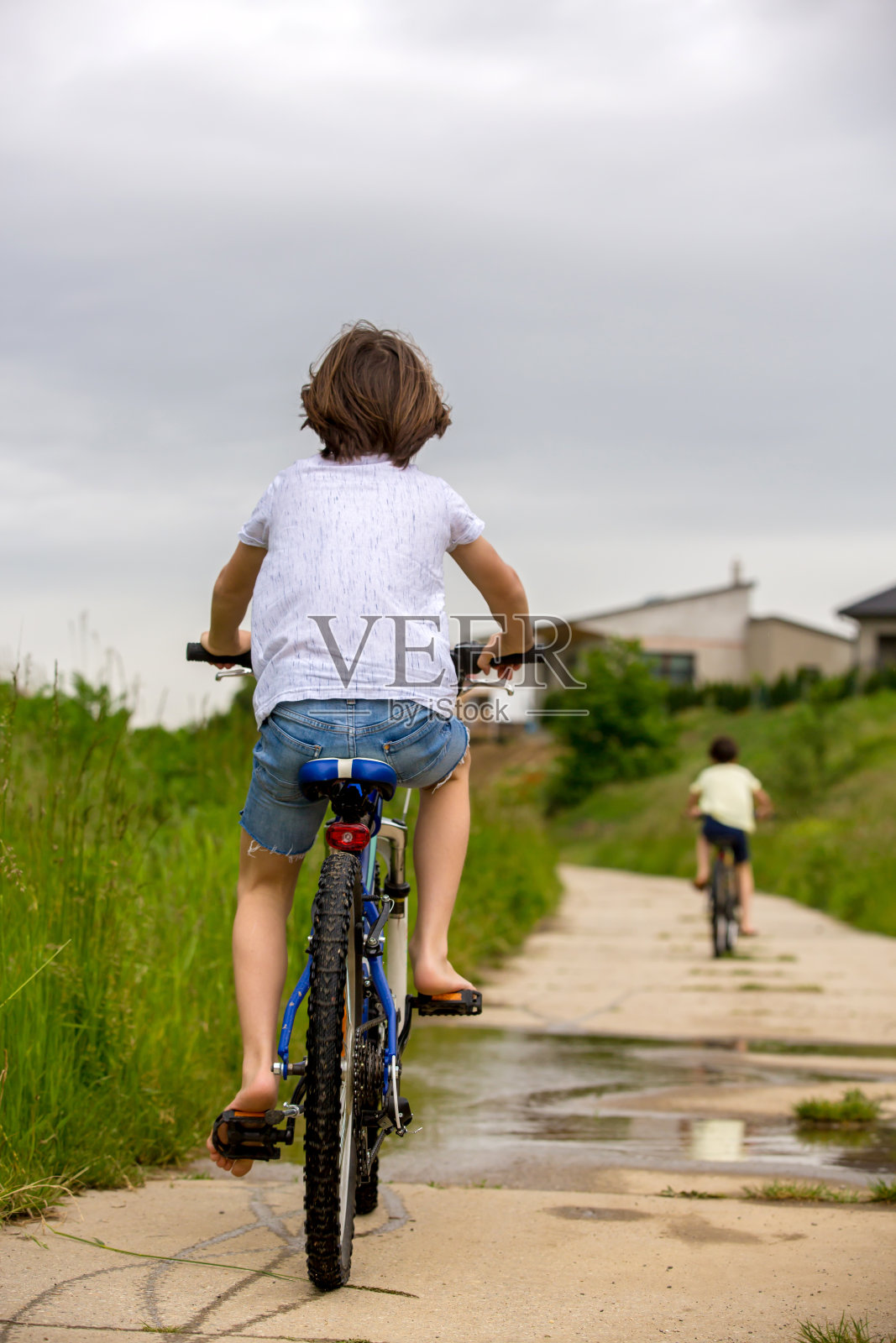 孩子，男孩，在泥泞的水坑里骑自行车，夏天的时候照片摄影图片