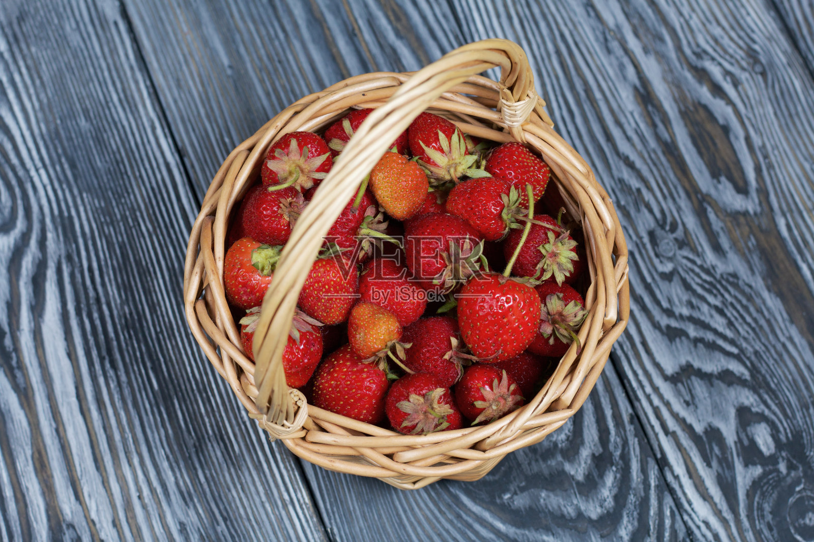 柳条篮子里装着成熟的红草莓。以黑白松木板为背景。2020年收获。从上面。照片摄影图片
