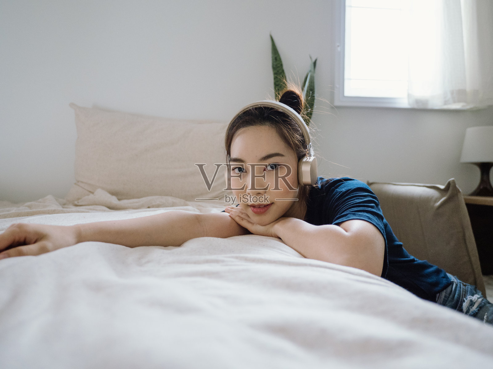 快乐的亚洲女人在卧室里用耳机听音乐。照片摄影图片