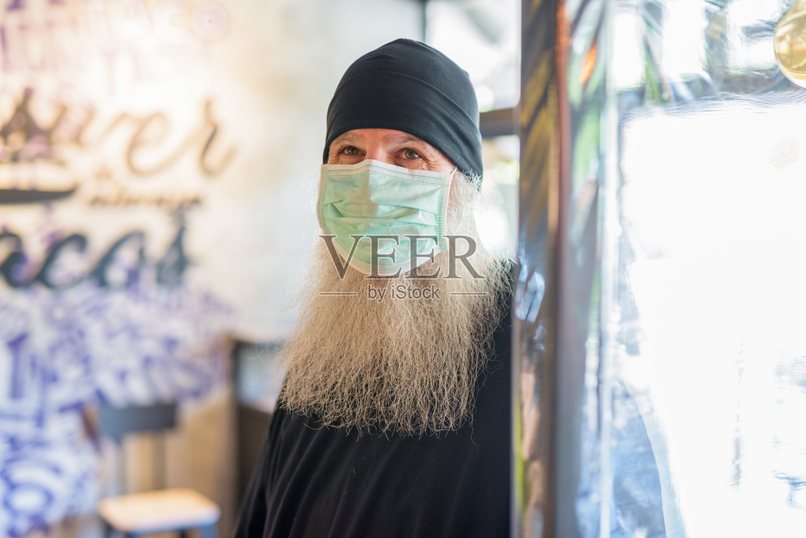 成熟的大胡子嬉皮士戴着面具在咖啡店里成为新常态照片摄影图片