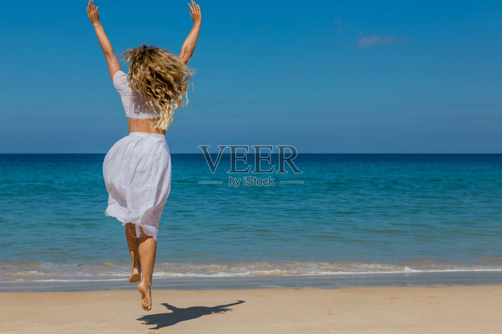 年轻漂亮的女孩穿着白色的衣服沿着海边的沙滩散步照片摄影图片