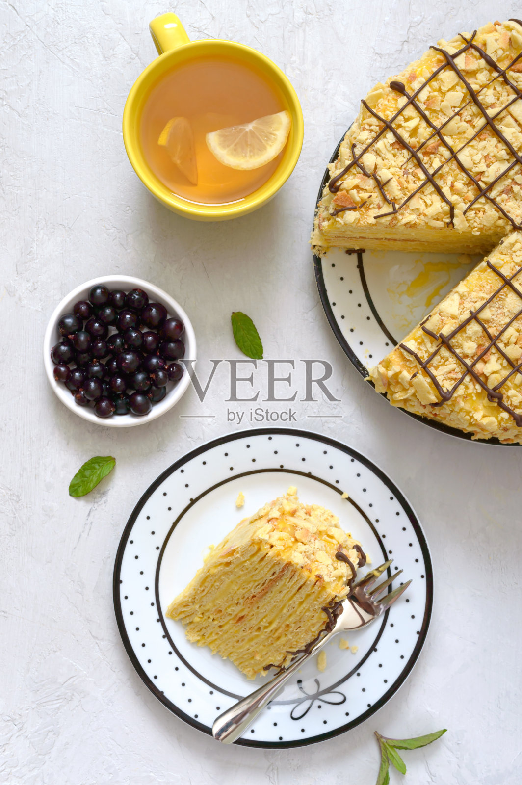 经典的拿破仑蛋糕。美味的节日甜点，酥皮和奶油冻装饰的新鲜浆果，一杯柠檬茶。前视图照片摄影图片