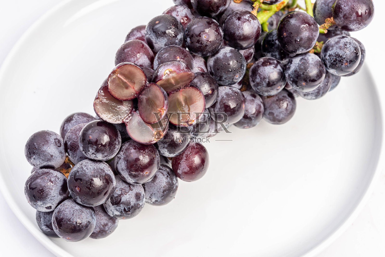 巨峰饱满的巨峰葡萄(巨大的山葡萄)孤立在一个滴水的盘子里，甜甜的，美味的。照片摄影图片