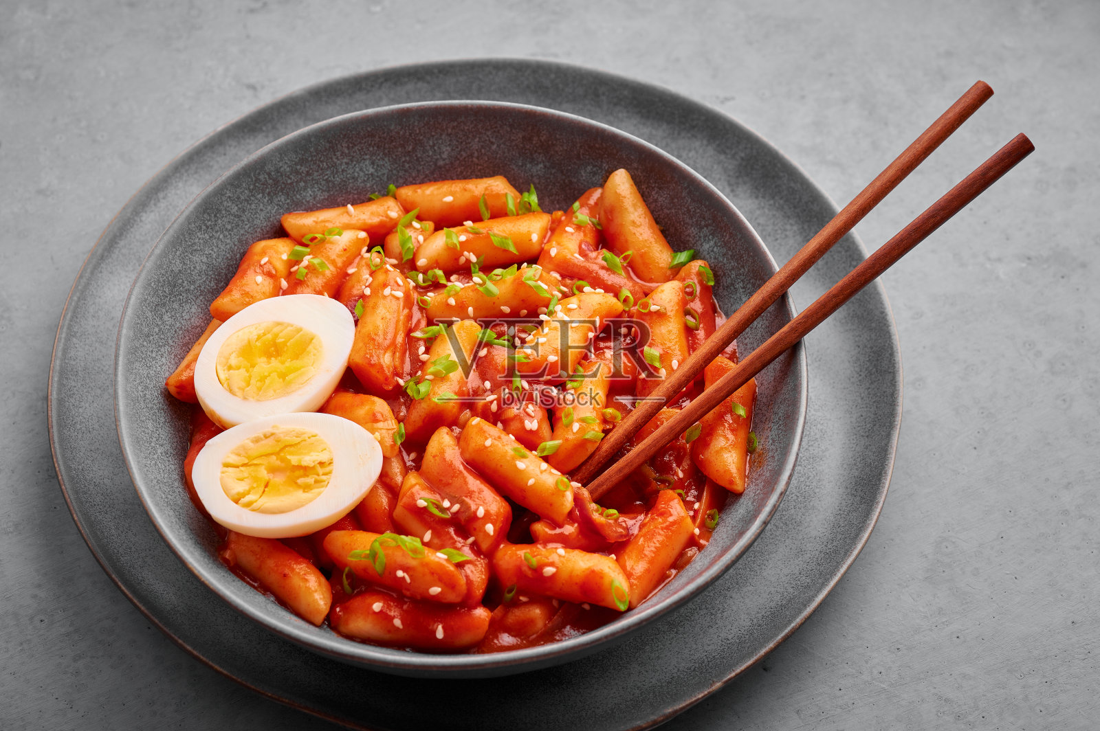 在水泥桌上的灰碗里放着鸡蛋。年糕是一道韩国菜，配上年糕。亚洲食品。照片摄影图片