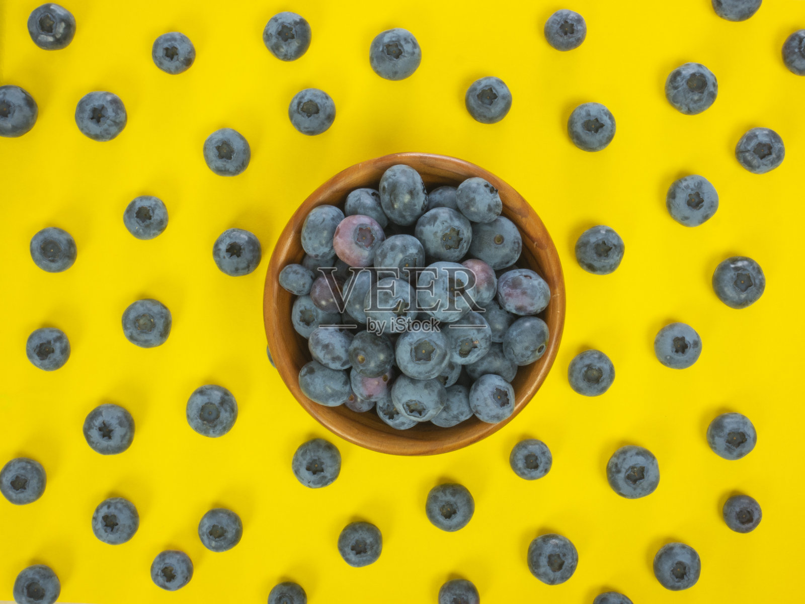 一个装满蓝莓的木碗，背景上散落着蓝莓。照片摄影图片