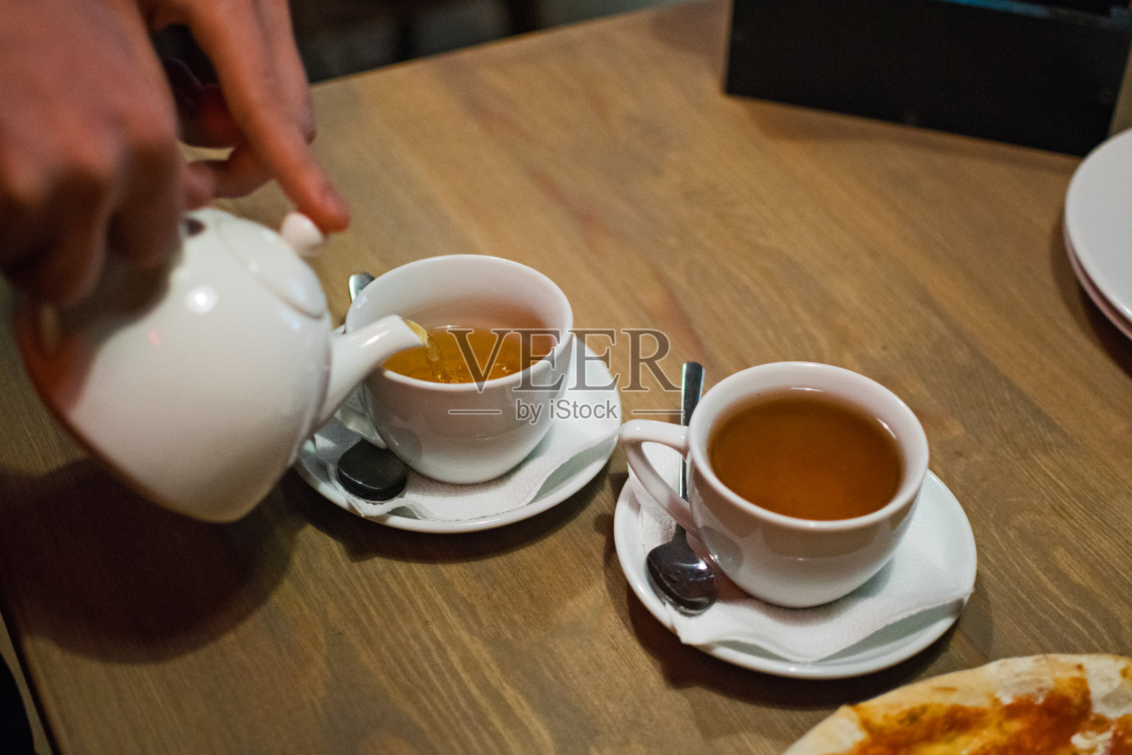 男人把茶从茶壶里倒进木桌上的白色杯子里。男人用手倒热腾腾的新茶。照片摄影图片