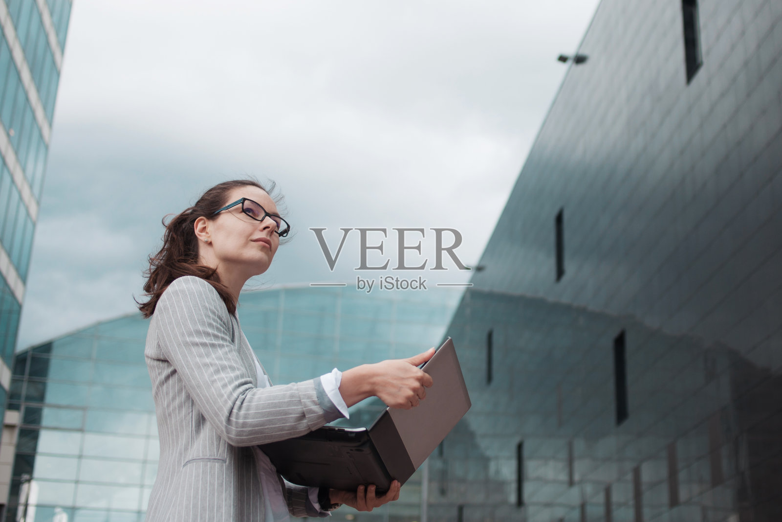 事业成长与抱负，理念。在商务中心的背景上，年轻的女商人手里拿着一台笔记本电脑。照片摄影图片