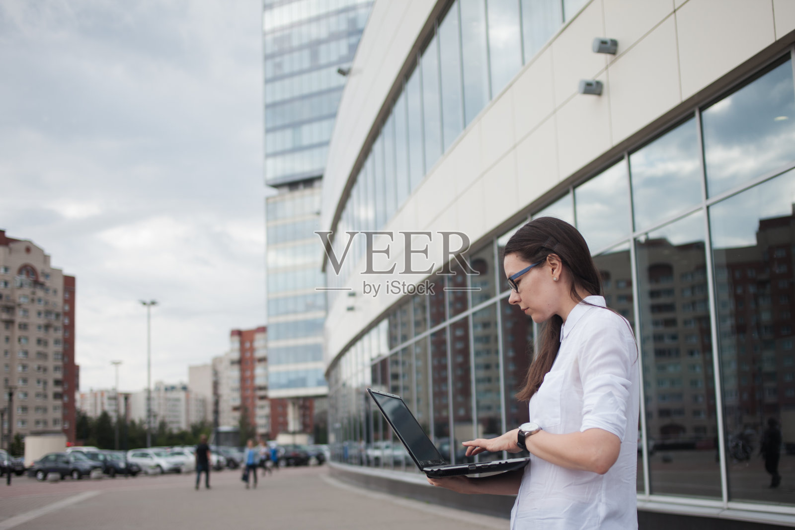 事业成长与抱负，理念。在商务中心的背景上，年轻的女商人手里拿着一台笔记本电脑。照片摄影图片