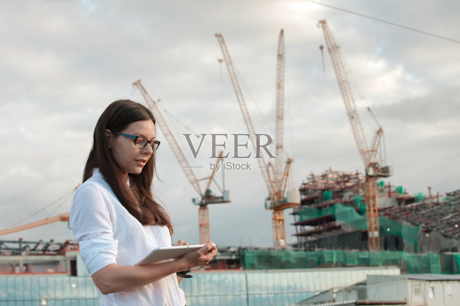 建筑师在施工现场进行监督。年轻的女工程师手里拿着平板电脑。照片摄影图片