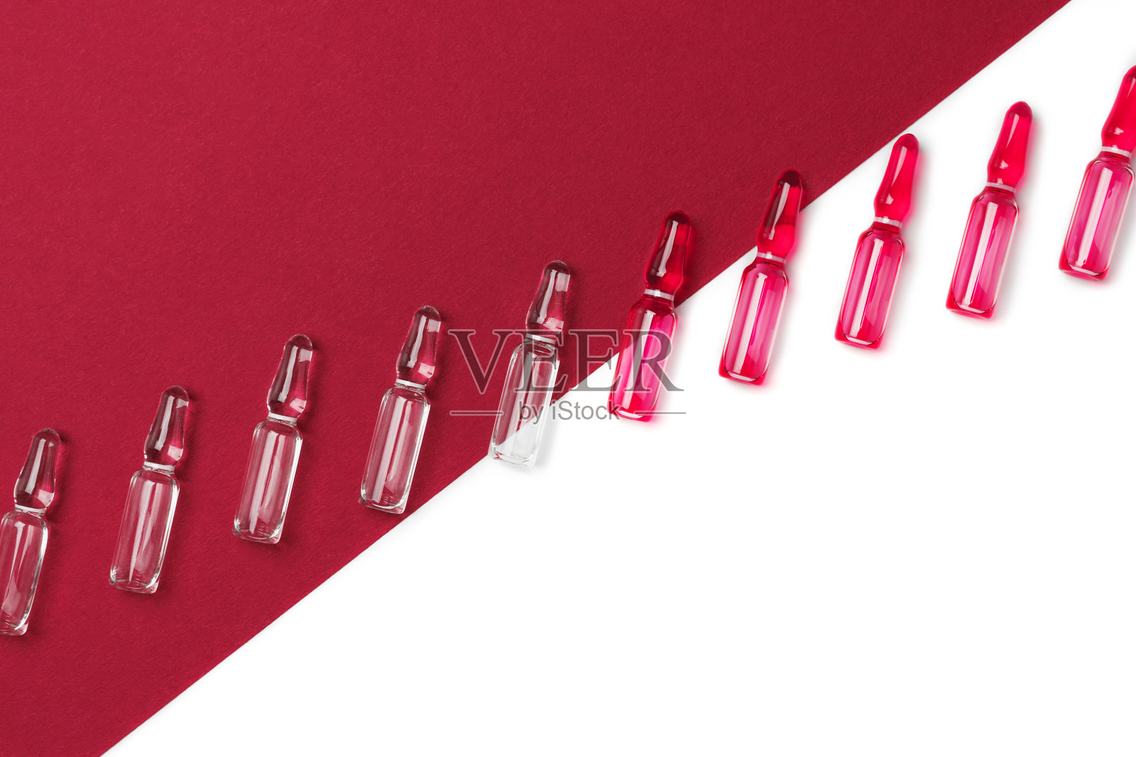 注射用安瓿的对角线，红色透明液体，背景为分离的白色和暗红色。医学、保健和药学概念。冠状病毒的概念。照片摄影图片