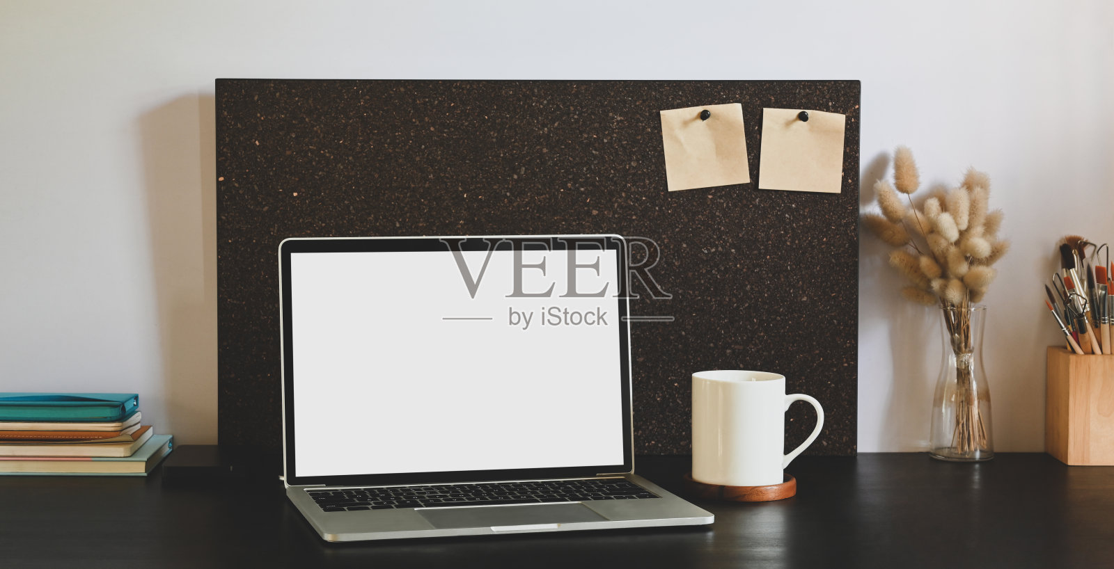 白色的空白屏幕电脑笔记本电脑放在黑色的办公桌上，周围是咖啡杯，静止，玻璃花瓶里的野草和一堆笔记本电脑。照片摄影图片