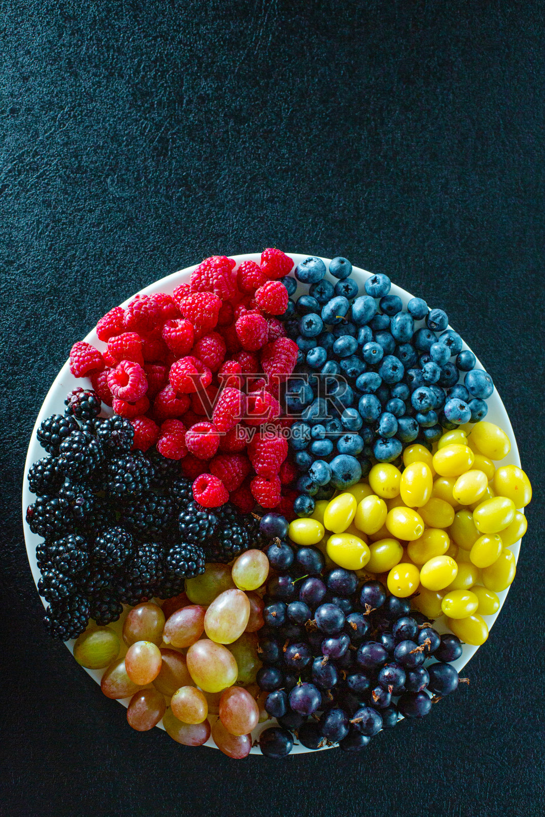 将有颜色的浆果混合在一个由三角形划分的圆盘子里。时尚的布局有用的夏季浆果维生素。照片摄影图片