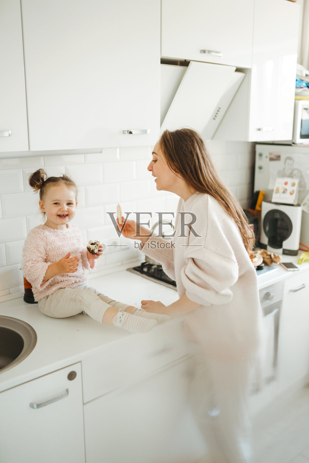 妈妈和小女儿在阳光明媚的厨房里玩得很开心。照片摄影图片