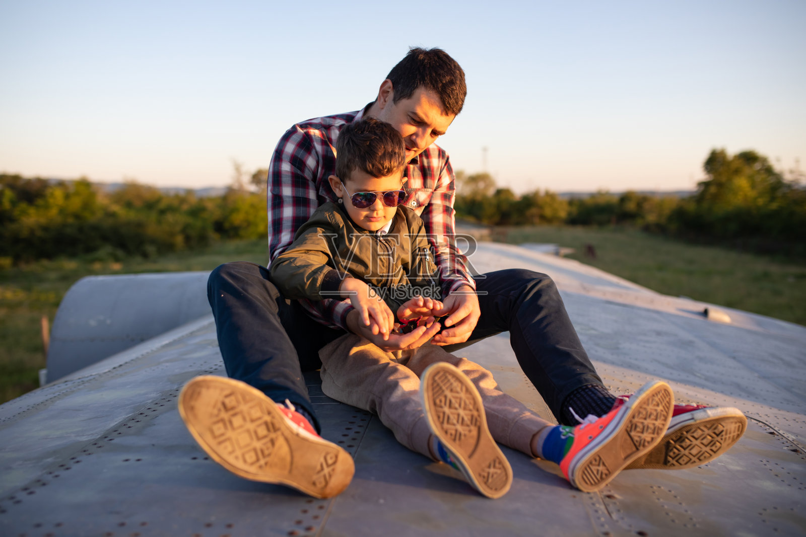 一个小男孩坐在他父亲的两腿之间在一架退役的飞机上照片摄影图片