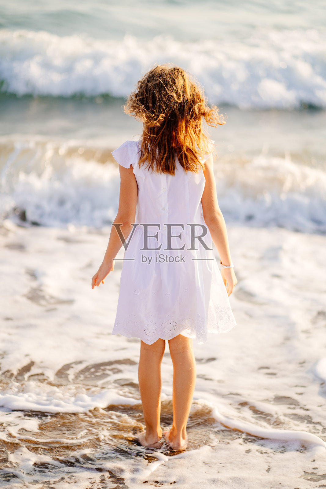 穿着白色裙子的女孩在海浪和大风的海边散步和玩耍。照片摄影图片