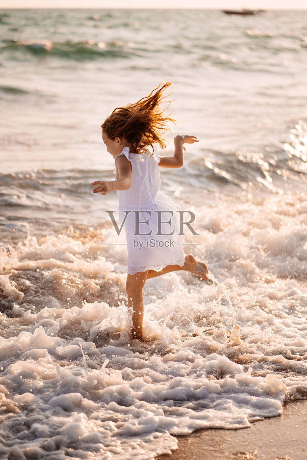 穿着白色裙子的女孩在海滩上跳跃着穿过海浪。走海运。假期。照片摄影图片