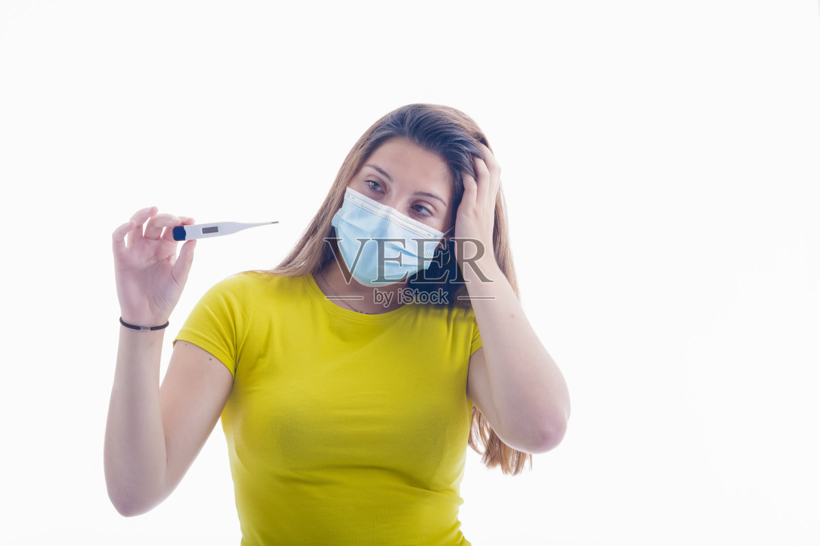 一名年轻女子戴着外科口罩，左手放在头上检查电子温度计照片摄影图片