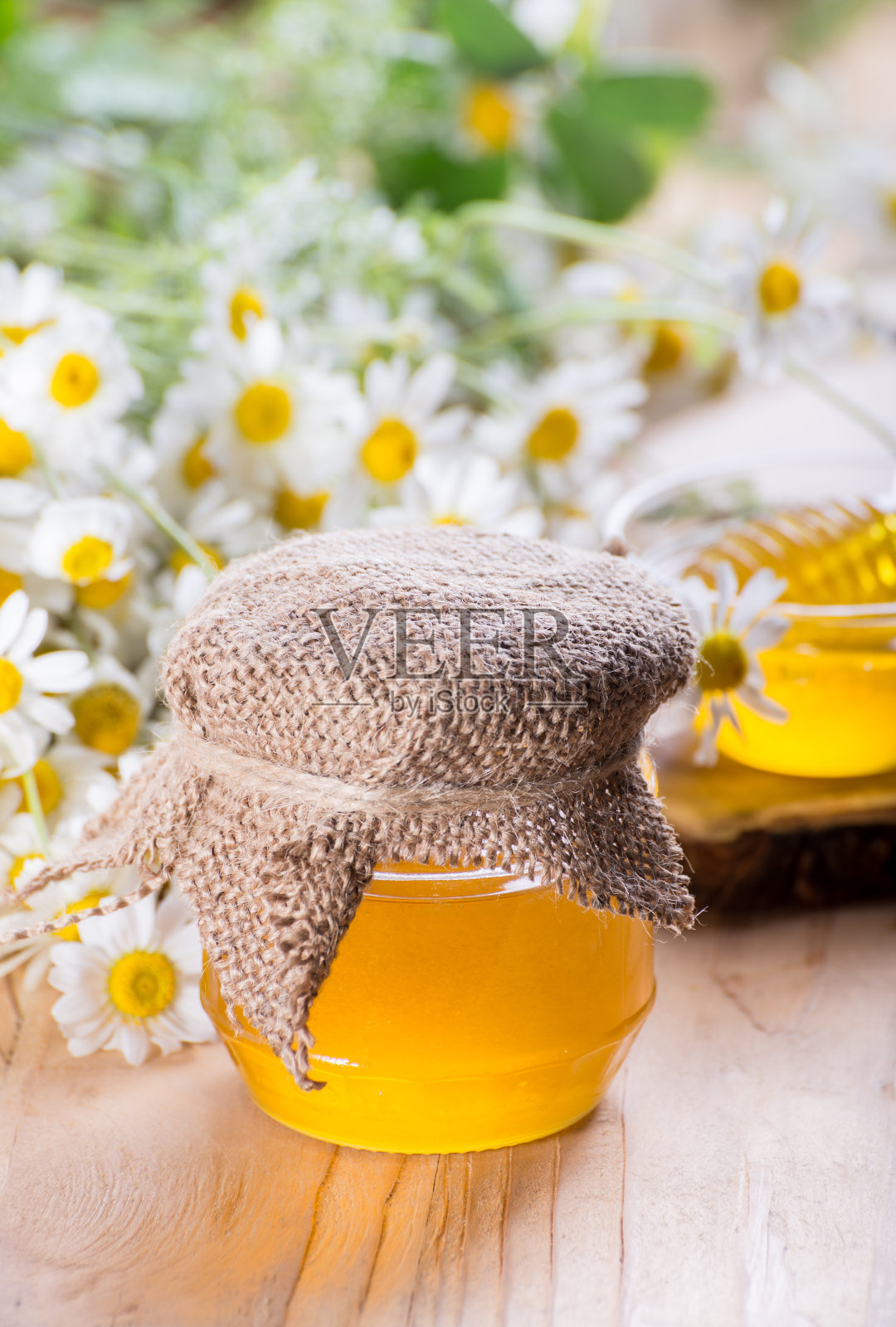 甜美的春天草本蜂蜜在罐子和小玻璃碗与蜂蜜勺。芳香的蜂蜜和新鲜的洋甘菊花组成。照片摄影图片