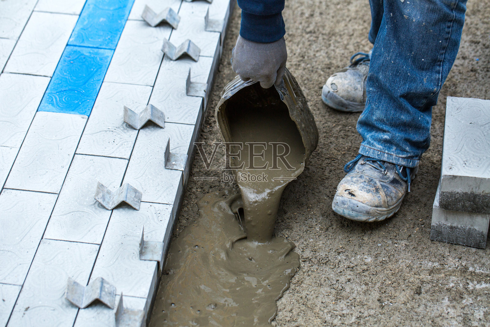 铺装工程。在人行道上安装混凝土摊铺机。工人将混凝土砂浆倒在预先准备好的表面上。照片摄影图片