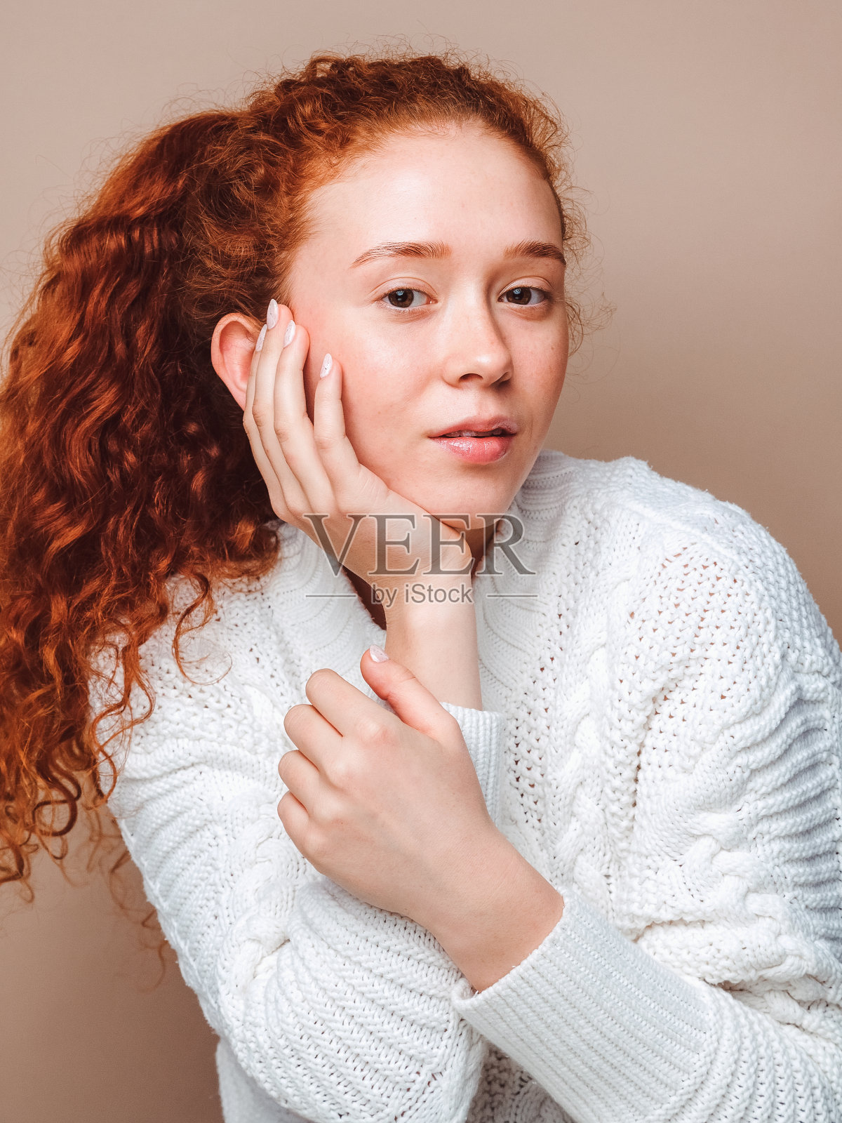 漂亮的女孩，红色长发，小雀斑，棕色眼睛，穿着一件白色毛衣。在米色背景上的工作室拍摄，没有修饰，没有化妆。照片摄影图片
