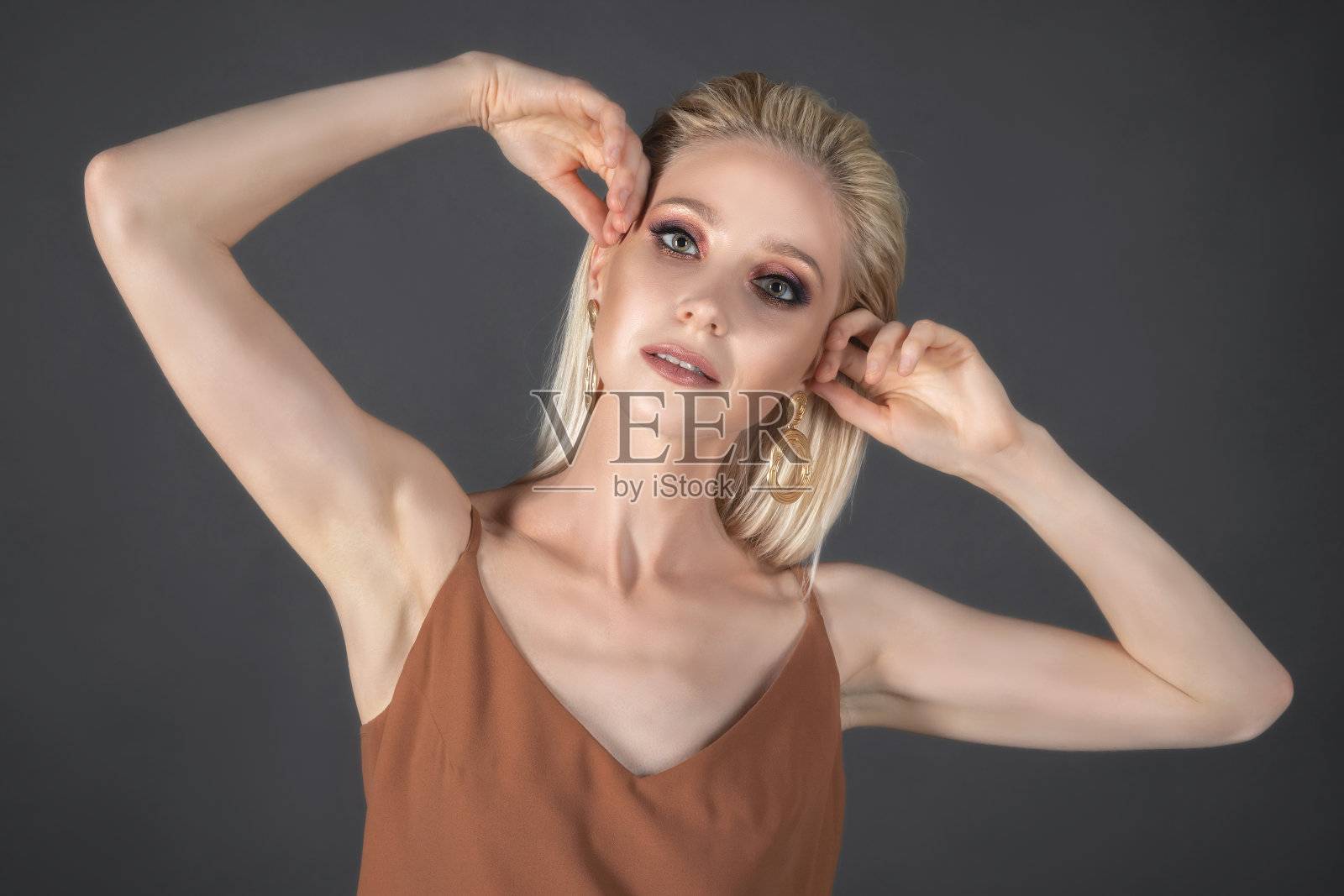 美丽的时尚模特与长长的金发和手臂在一个深灰色的背景下摆姿势。发型和化妆都在美容院做照片摄影图片