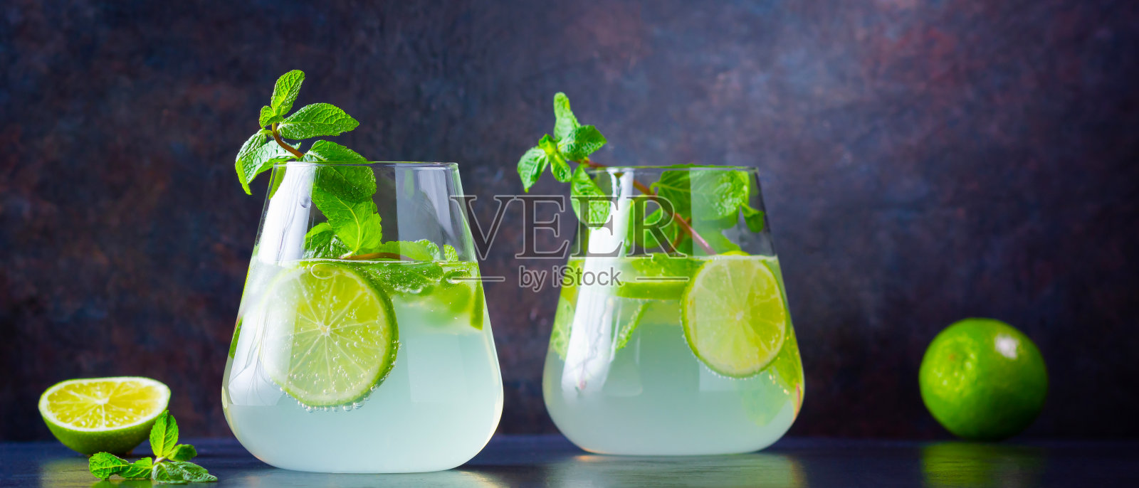 莫吉托鸡尾酒，柠檬和薄荷杯。两杯莫吉托，深色背景。清新的薄荷鸡尾酒配青柠。注入水照片摄影图片
