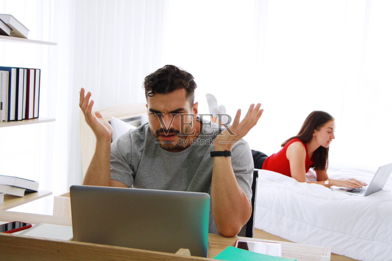 严肃的白人男人和妻子在卧室里用笔记本电脑在社交媒体技术上工作。在家工作和家庭生活方式度假的概念。照片摄影图片