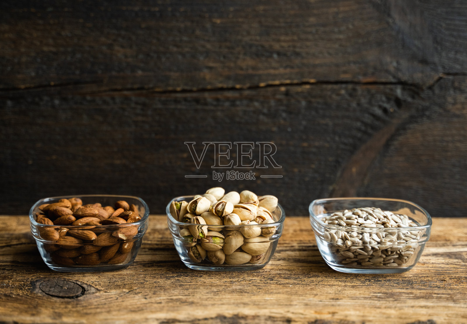 杏仁、开心果和葵花籽装在一个小盘子里，放在一张老式的木头桌子上。坚果是一种健康的素食蛋白质和营养食物。在粗糙的旧木头上的坚果。照片摄影图片