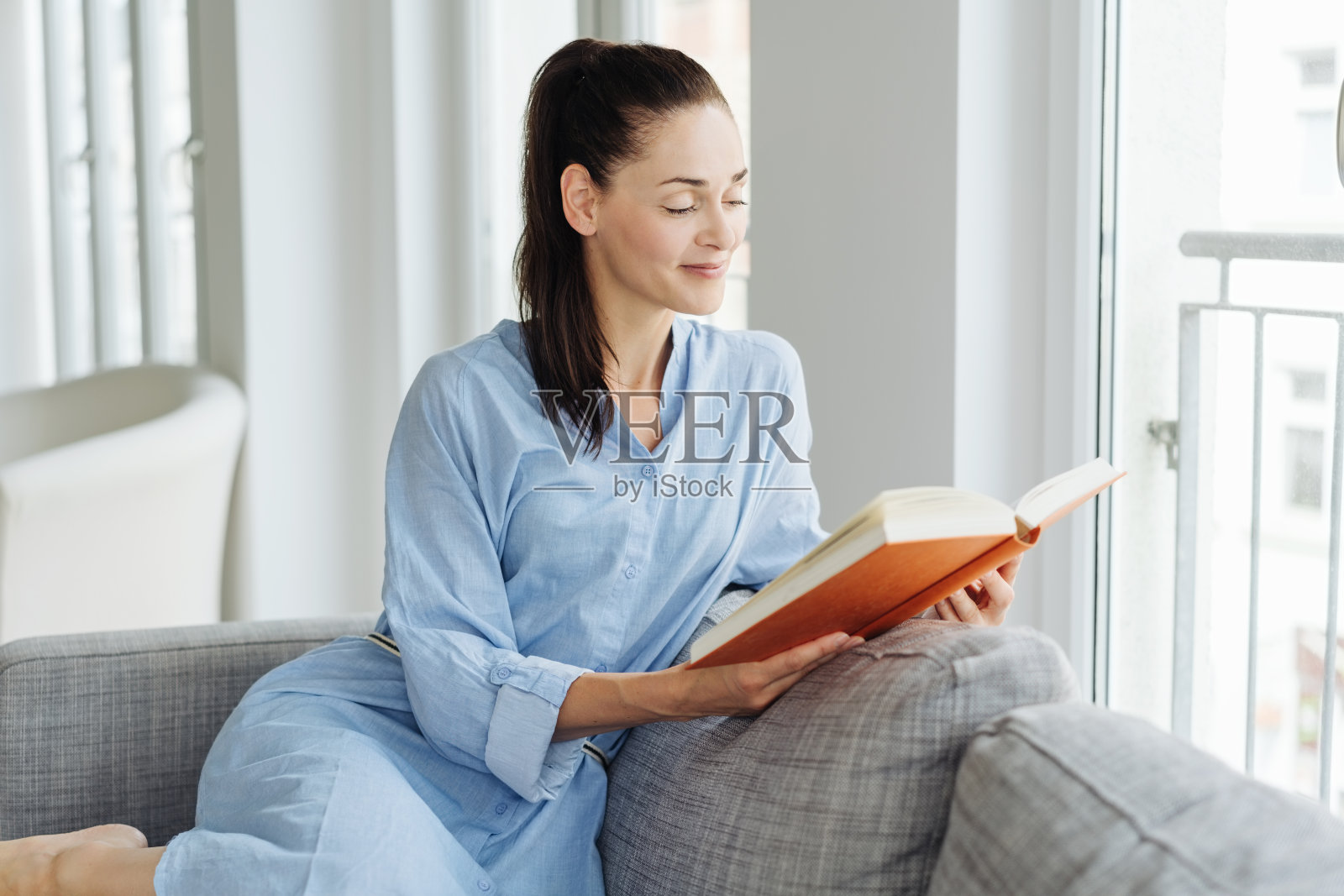 一个年轻女子坐在沙发上看书照片摄影图片