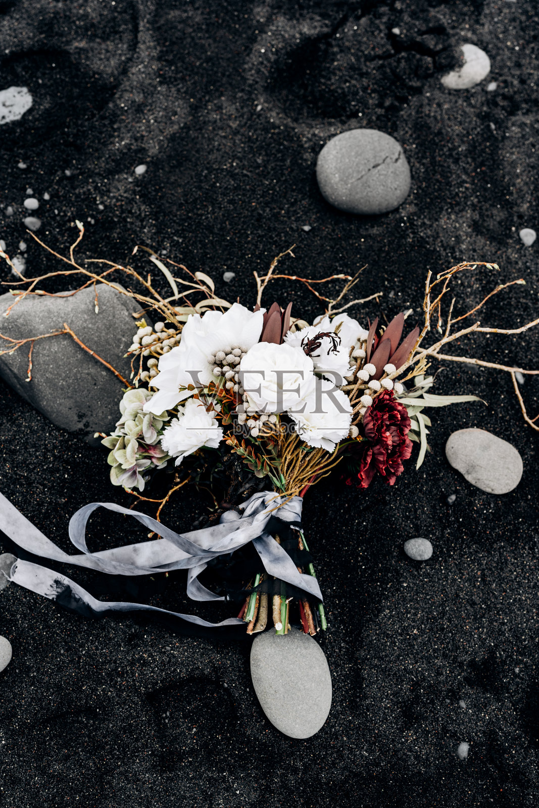 冰岛黑色沙滩上的新娘花束，由白玫瑰、百合、勃艮第丁香、protea、干枝、布鲁尼和带着灰色和黑色丝带的leucadendron组成照片摄影图片