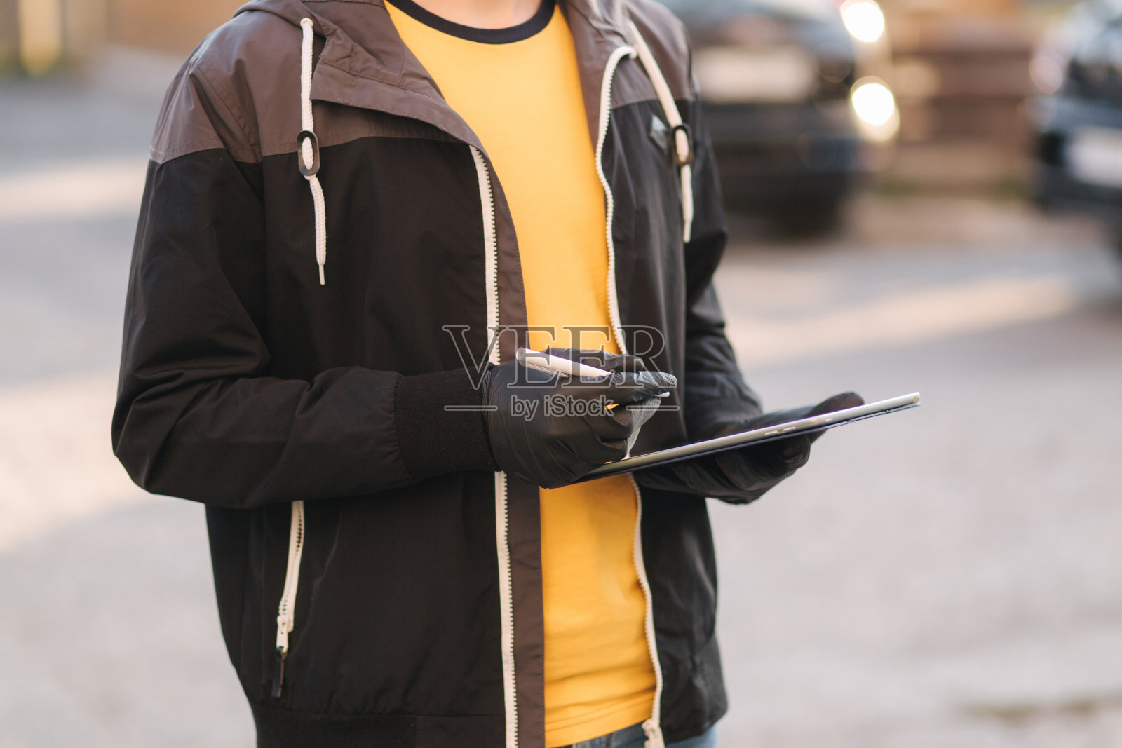 智能外卖服务。戴医用口罩和手套的人用药片检查运送。客户在家里接受快递员的快递。带着平板电脑的快递员，签到。交付的男孩。背景的汽车照片摄影图片