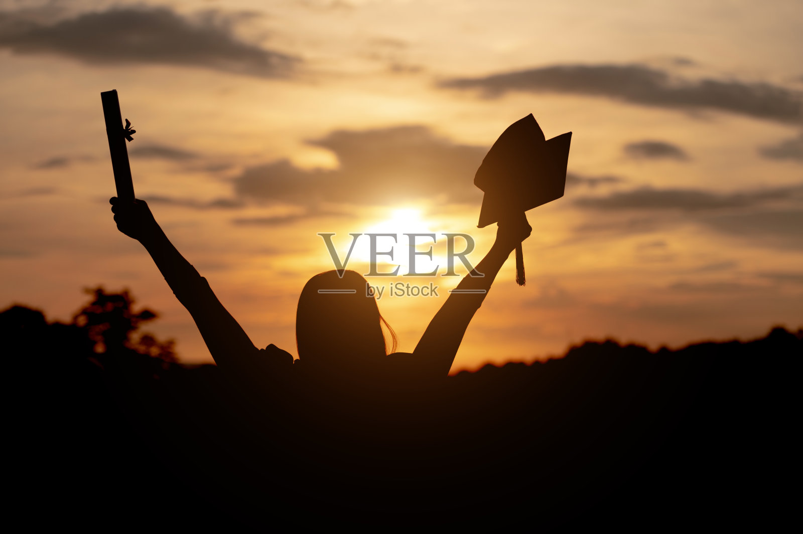 大学女毕业生穿着黑色长袍，戴着黑色帽子，看着夕阳照片摄影图片