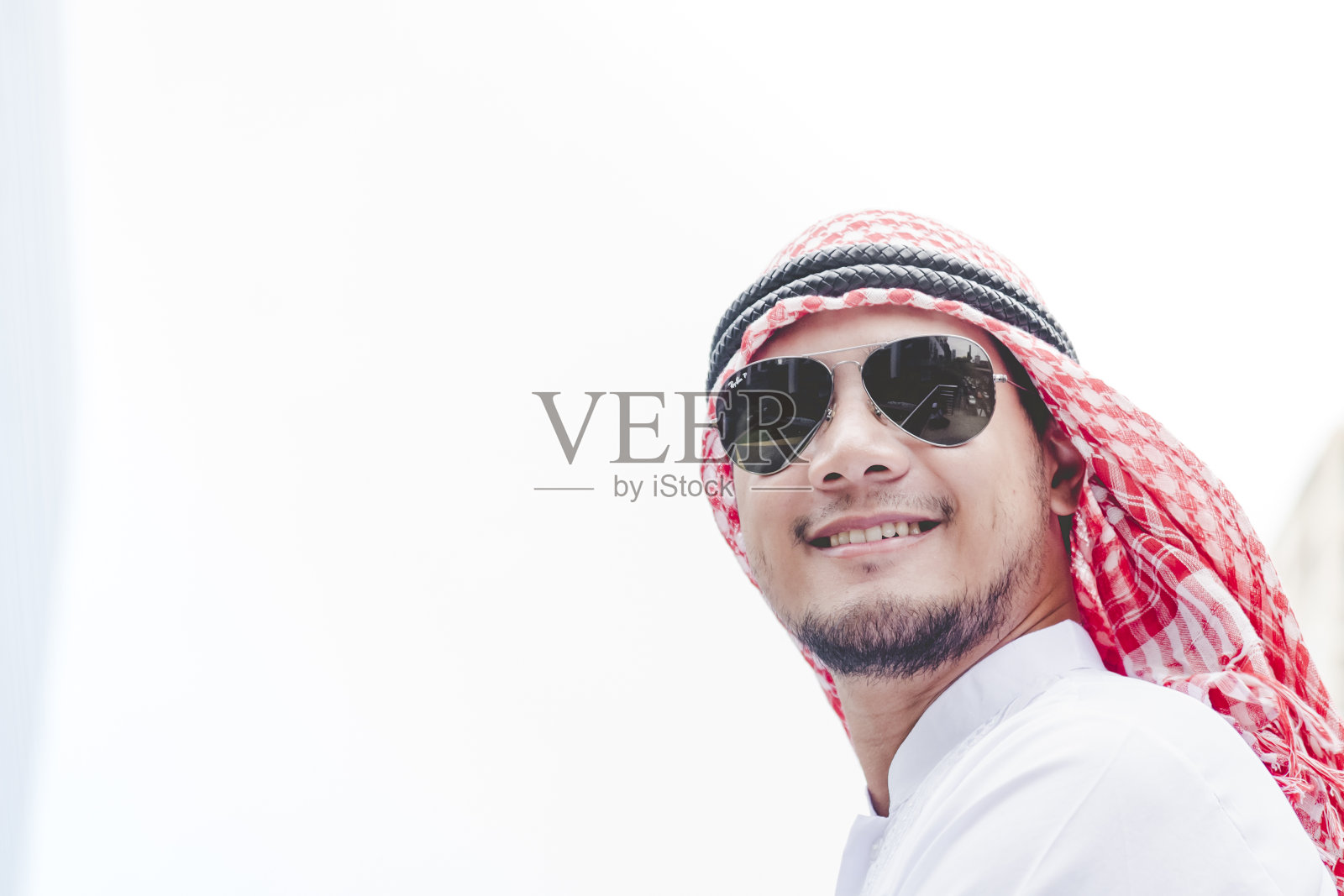 穿着穆斯林服饰的阿拉伯男人站在现代城市里，面带微笑照片摄影图片