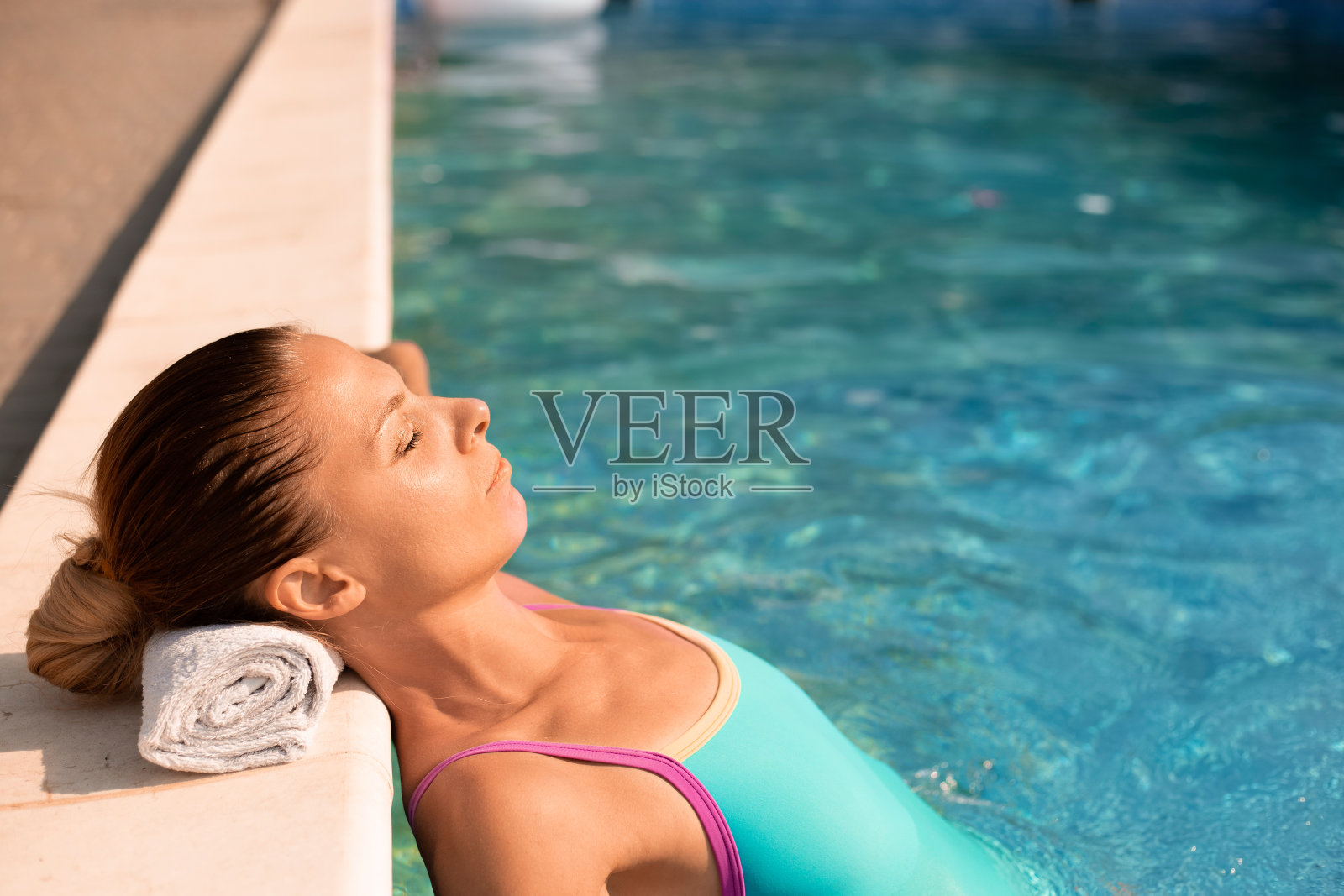 美丽的年轻女子正在室外游泳池里放松。美容美体护理，豪华酒店水疗度假，热带度假旅游。年轻的长发女子在游泳池里晒成金黄色。照片摄影图片