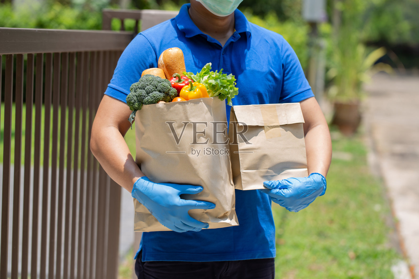 送餐员拿着装着食品的纸袋站在门前，送餐员戴着防护口罩和防护手套。疾病暴发、冠状病毒新冠肺炎大流行情况。照片摄影图片