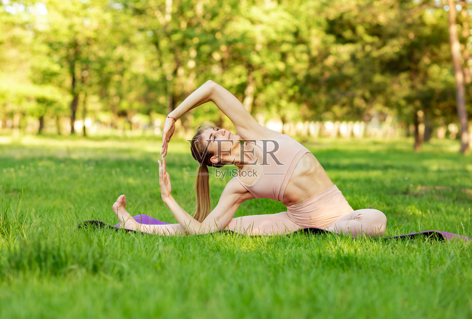 一名女子在绿树和草地的背景下练习瑜伽照片摄影图片