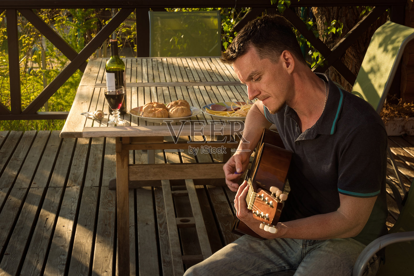 一个弹吉他喝酒的年轻人。Covid-19隔离。照片摄影图片