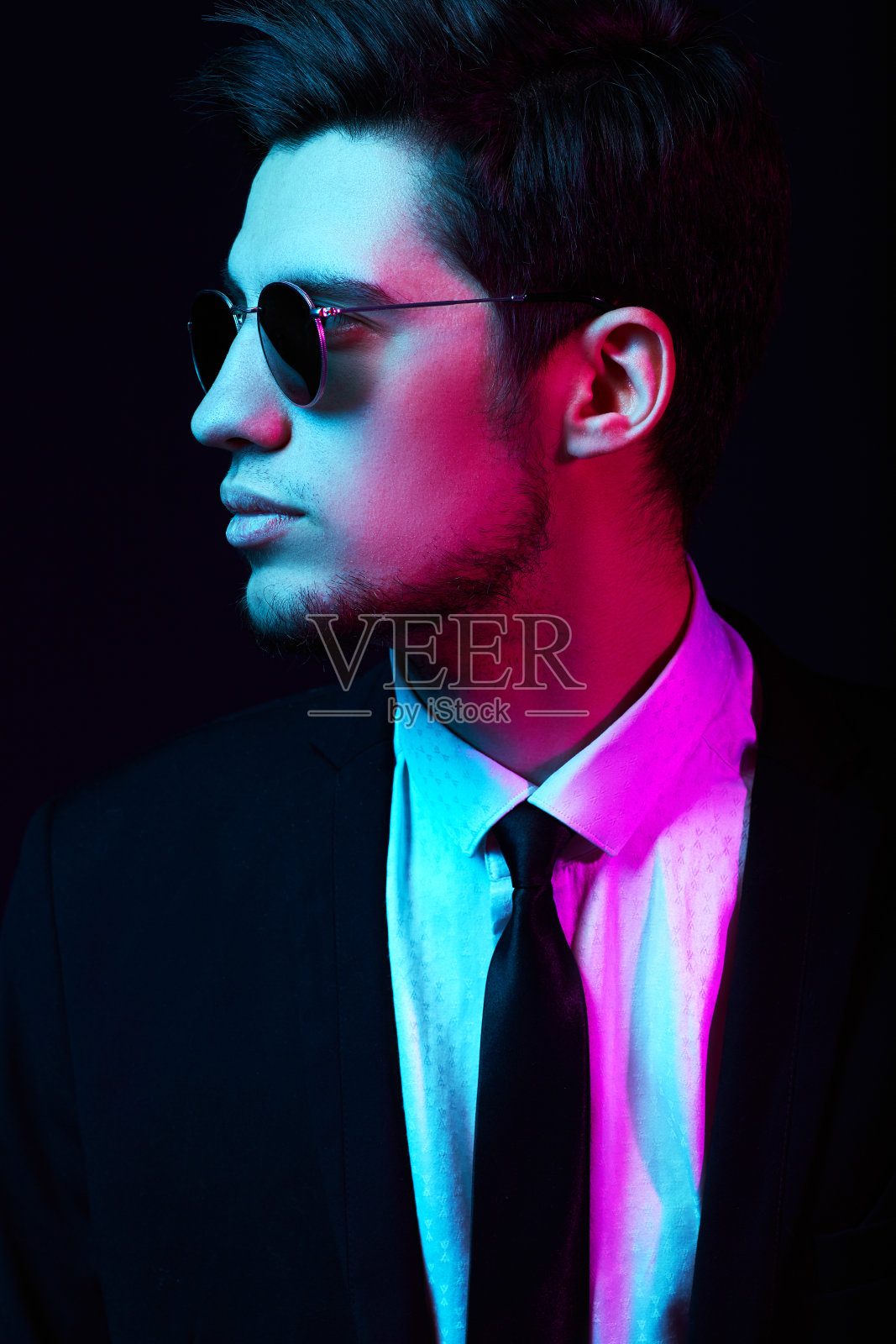 霓虹工作室的年轻男子肖像戴着时髦而优雅的太阳镜сostume。照片摄影图片