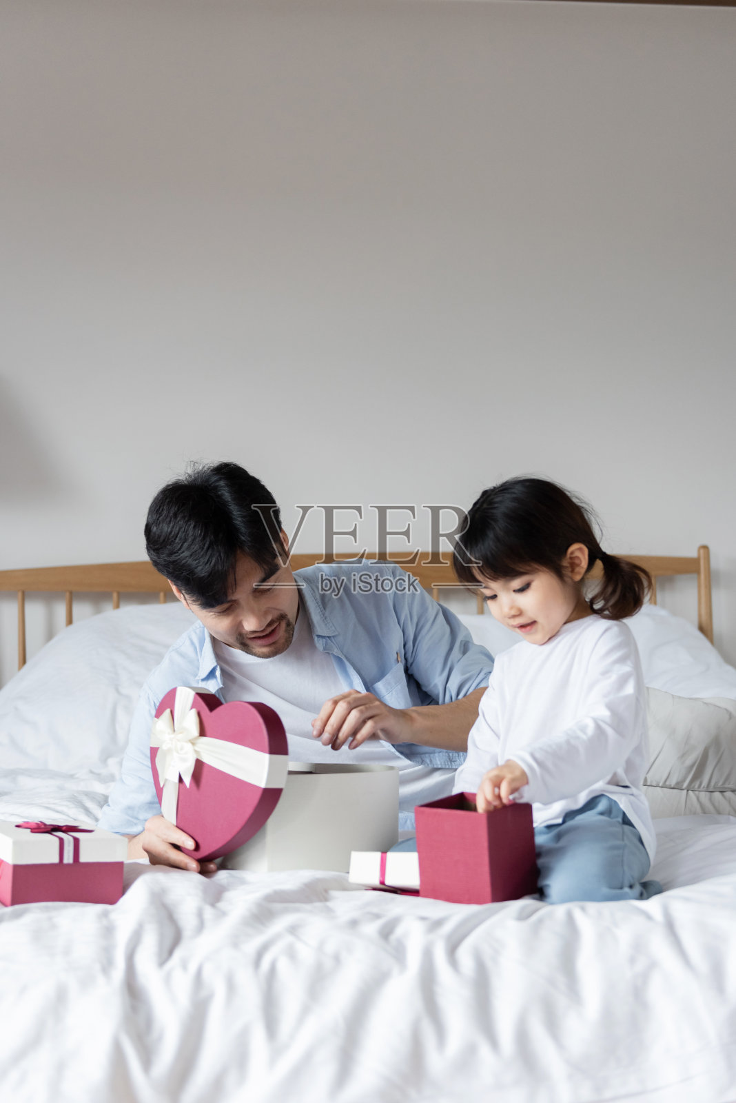 年轻的亚裔爸爸和女儿在床上拆礼物照片摄影图片