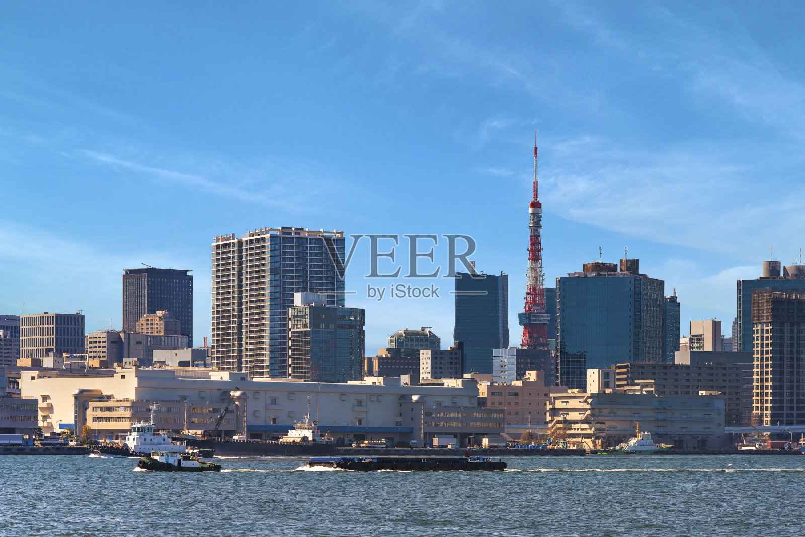 由拖船拖着的驳船在东京港航行，后面是东京塔。照片摄影图片