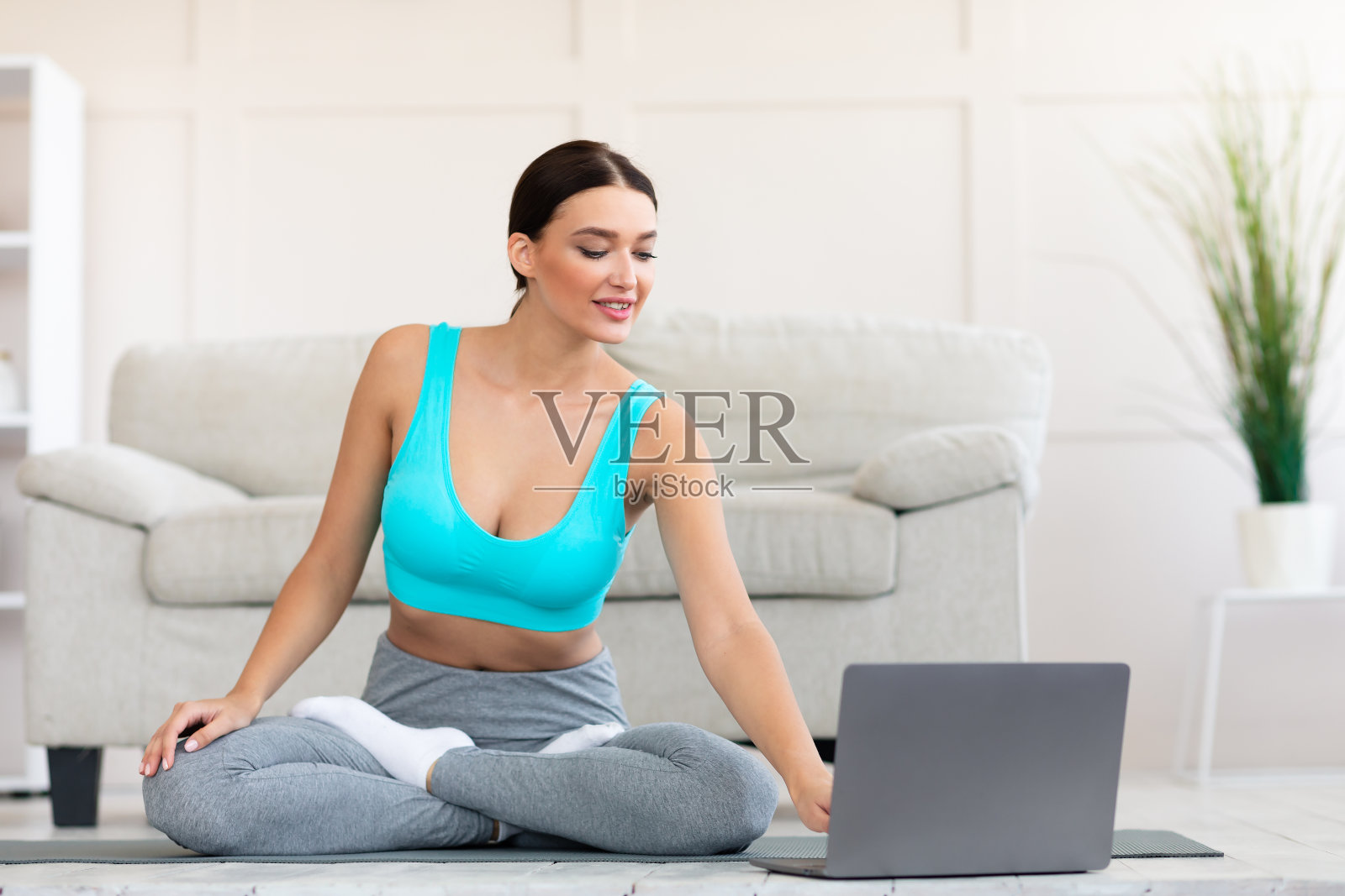 女孩坐在室内垫子上用笔记本准备做瑜伽照片摄影图片