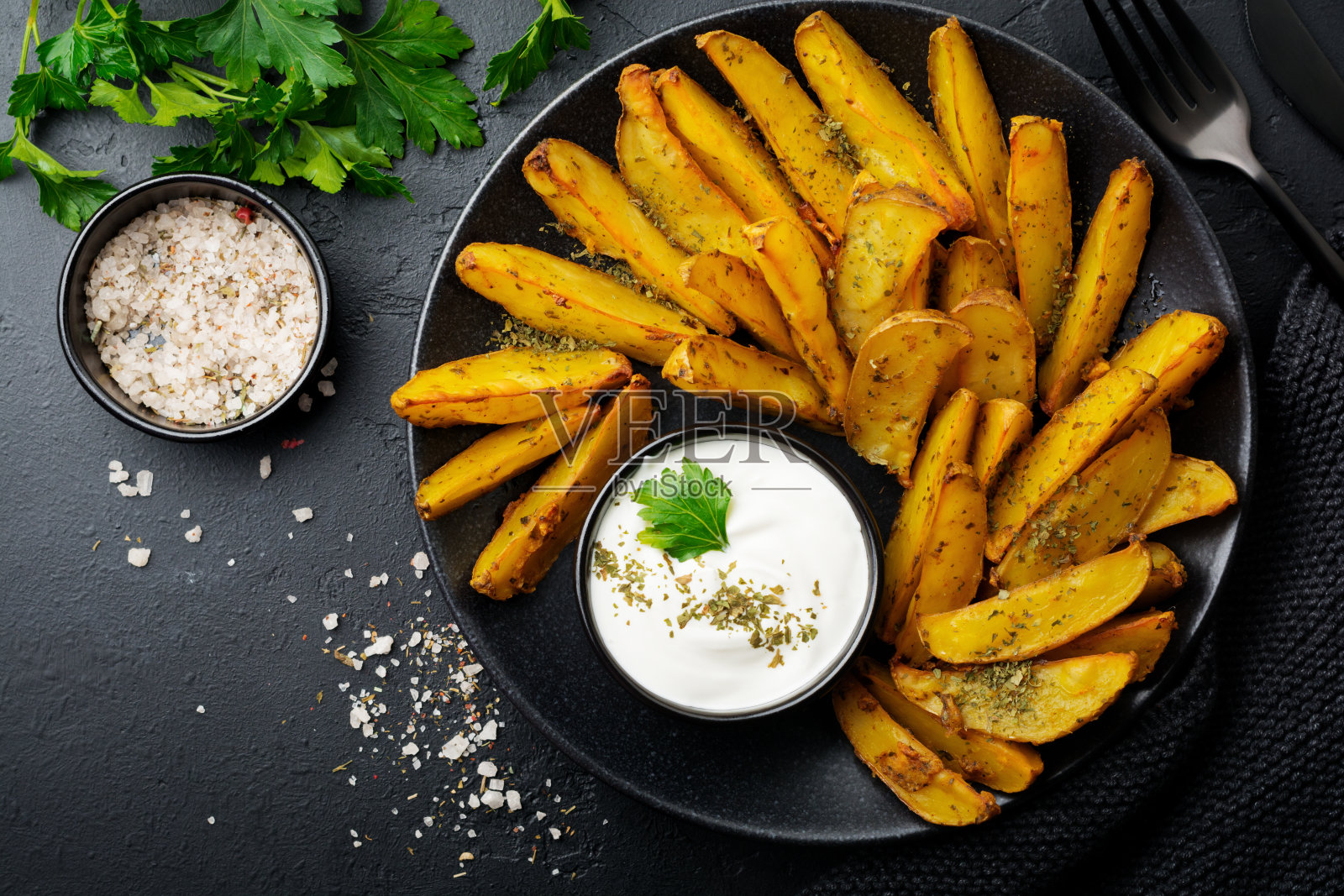烤土豆配青菜和酱料，放在黑色陶瓷盘中，背景为黑色混凝土或陶瓷。有选择性的重点。前视图。文本。照片摄影图片