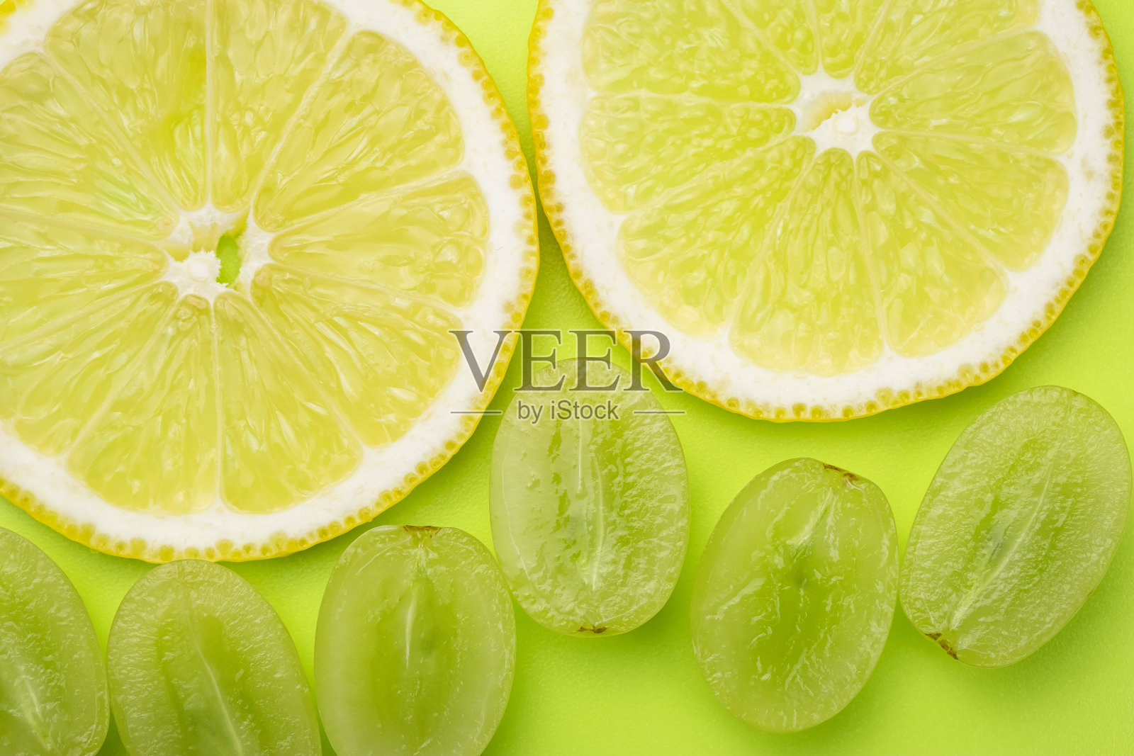 一片柠檬和白葡萄浆果在浅绿色的背景上。夏天鲜艳的壁纸，图案。绿色和黄色质地。照片摄影图片