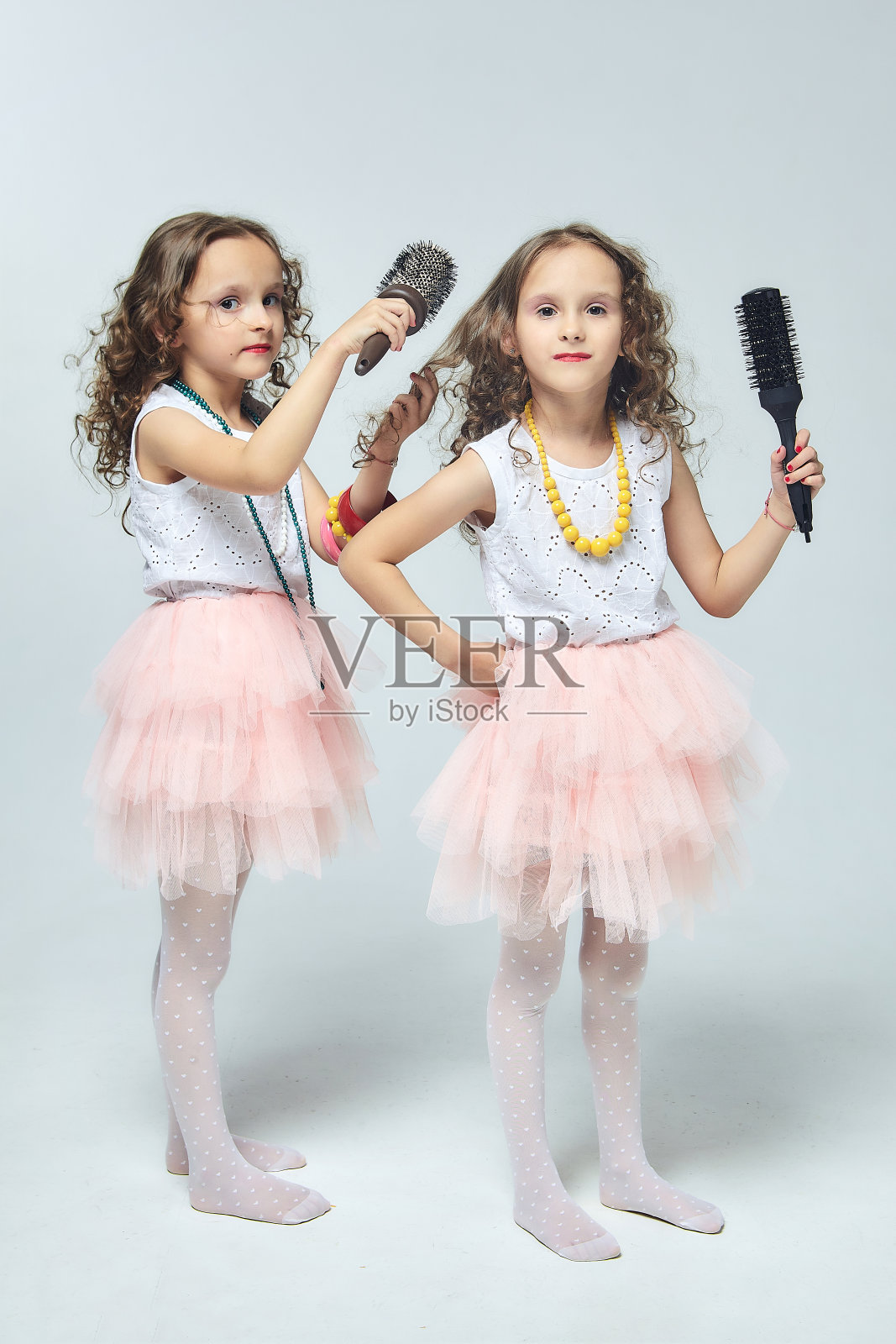 两个小女孩互相梳头。一对双胞胎姐妹对着梳子唱歌。白色背景照片摄影图片